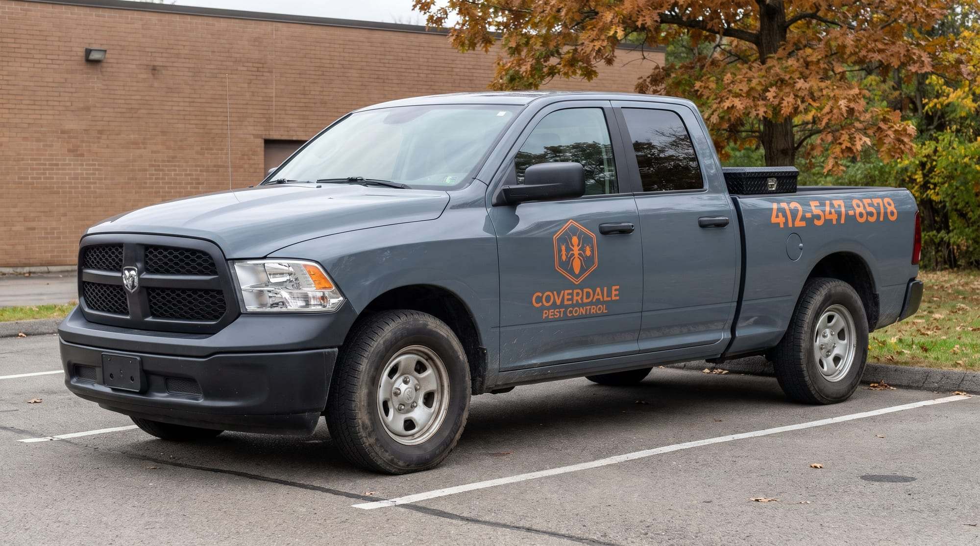 Slate gray Coverdale Pest Control pickup with the orange hexagon ant logo on the front door and 412-547-8578 on the bed, parked in a lot by a brick building
