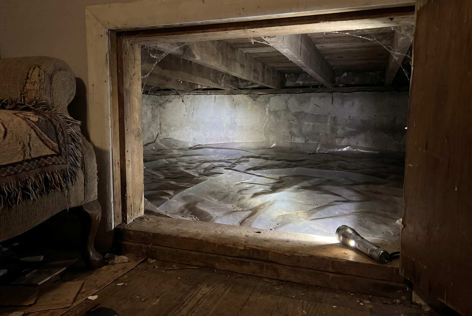 Flashlight resting on the sill plate at the opening of a low crawl space lined with plastic sheeting