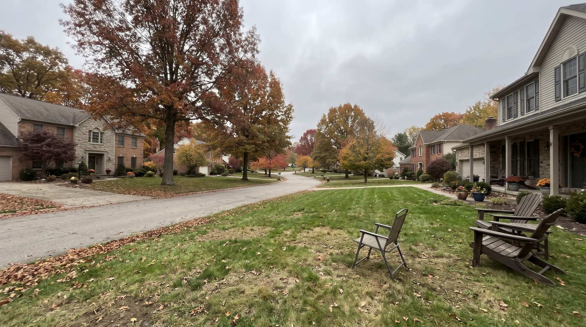 Curving residential street of brick and stone houses under oaks and maples in autumn color
